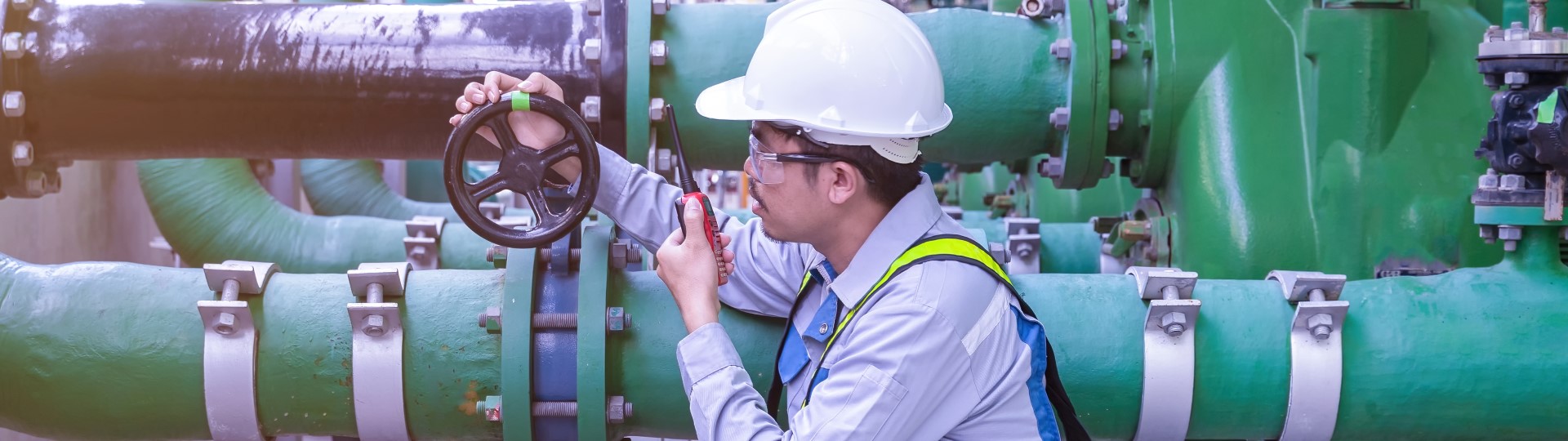 An engineer on a walkie talkie inspecting the valve of a pipe