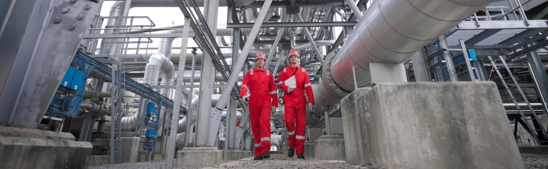 Two men in boiler suits and hard hats walking through a energy facility