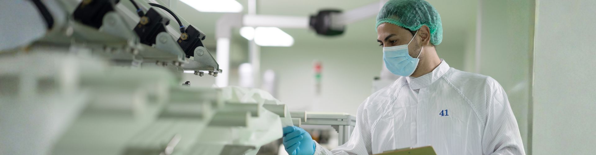 Pharmaceutical worker in sterile gear inspecting production line machinery