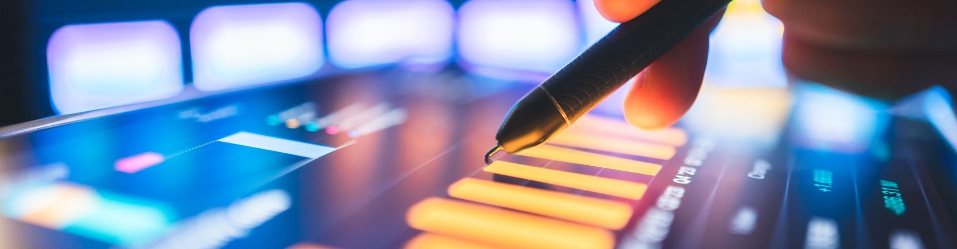 Close-up of a hand using a stylus on a digital tablet displaying financial data charts