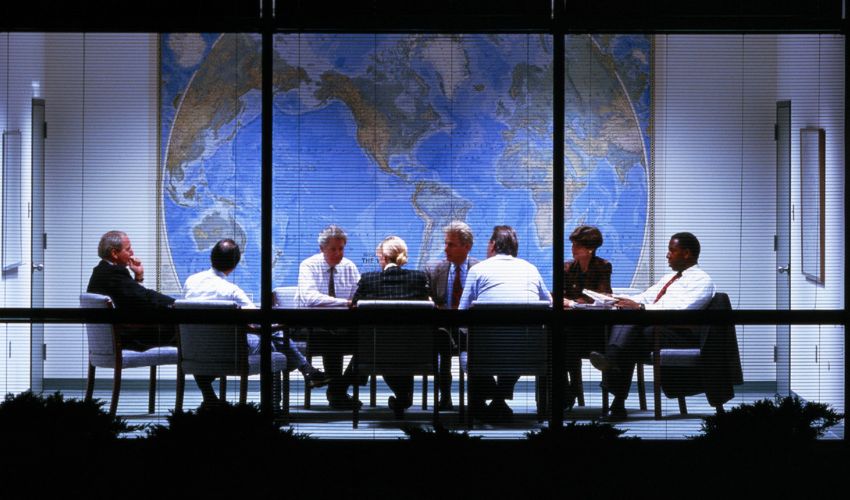 A group of professionals in a meeting room with a large world map on the wall