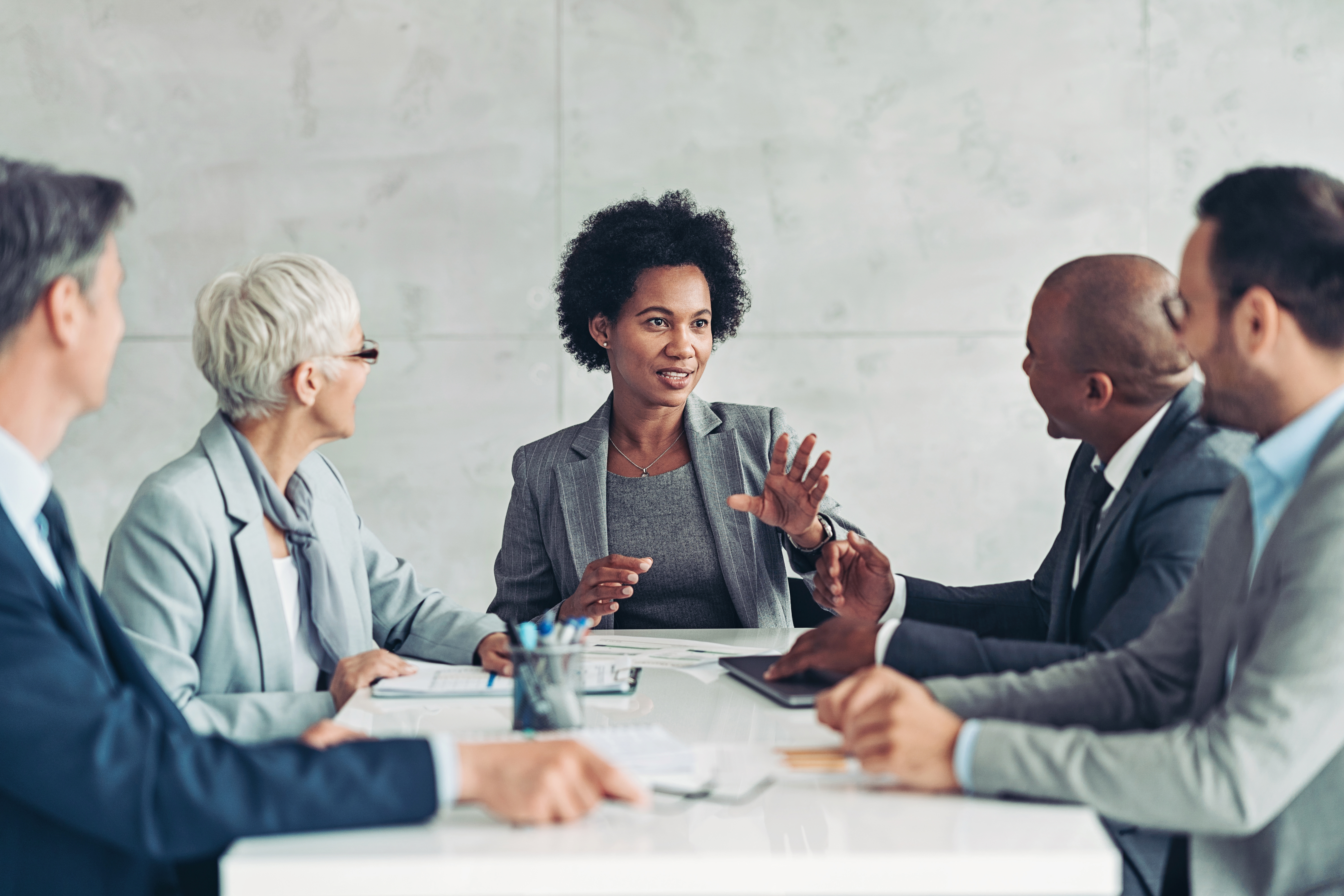 Five professionals in business attire having a collaborative meeting around a white table