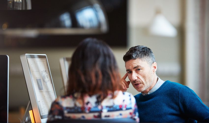 Man and woman talking in front of computers 