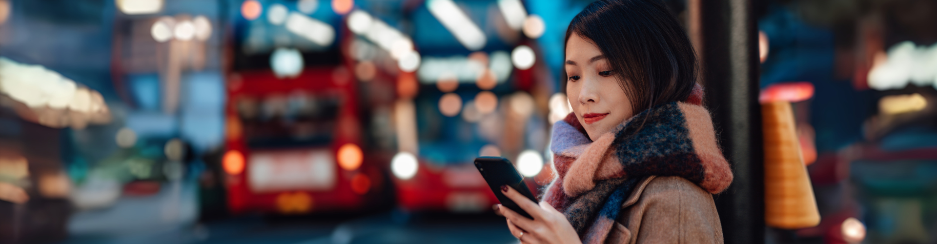 Women next to London bus stop looking at phone at night