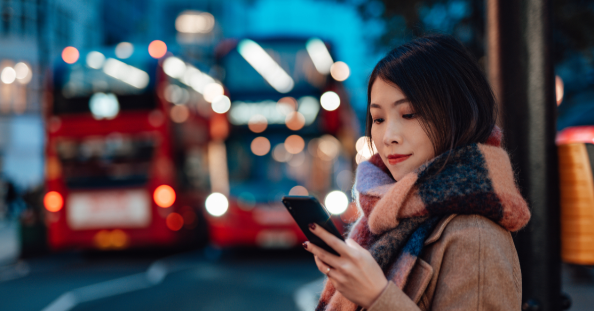 Women next to London bus stop looking at phone at night