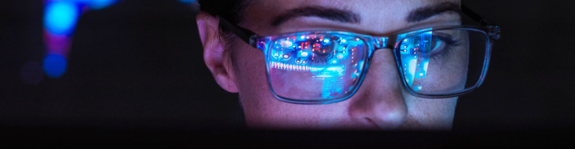 Woman in a dark room with screen monitor reflecting in her glasses