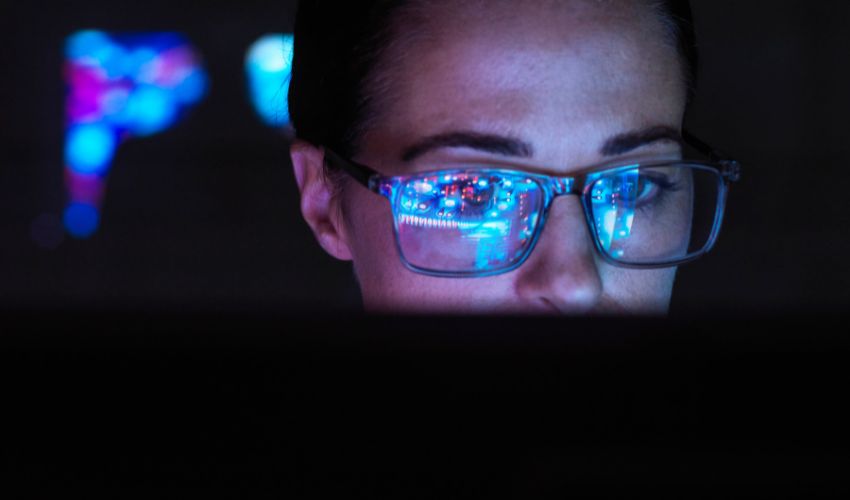 Woman in a dark room with screen monitor reflecting in her glasses