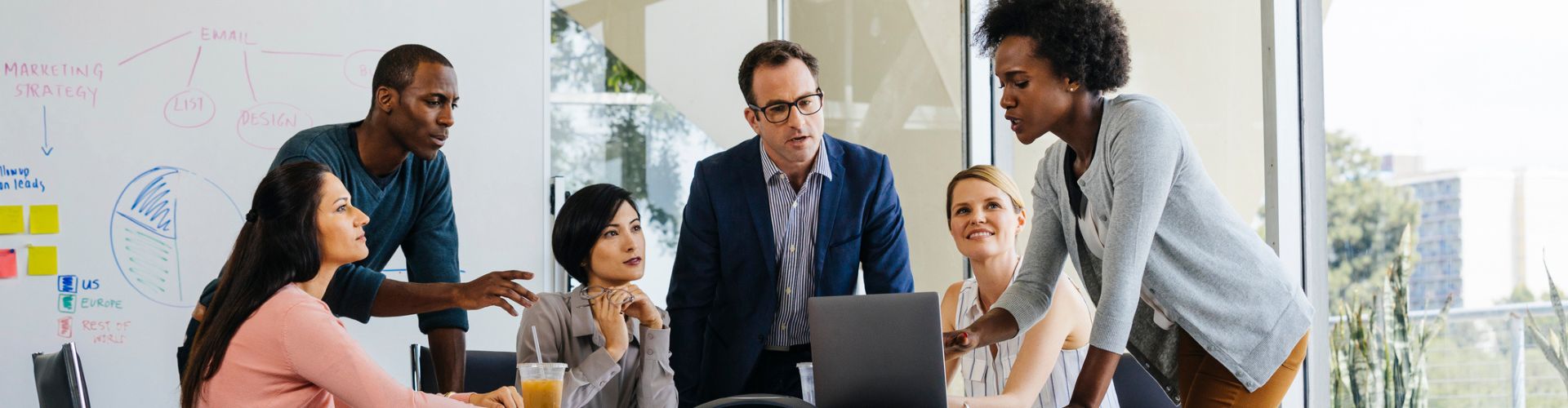 A diverse group of professionals collaborating around a laptop in a bright, modern meeting room