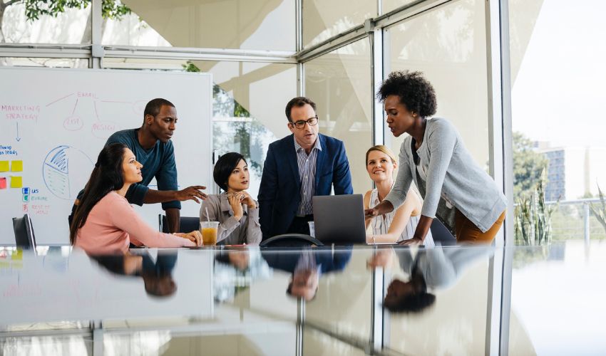 A diverse group of professionals collaborating around a laptop in a bright, modern meeting room