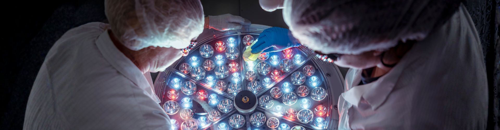 Scientists in protective gear working on a large, circular light-emitting technological device