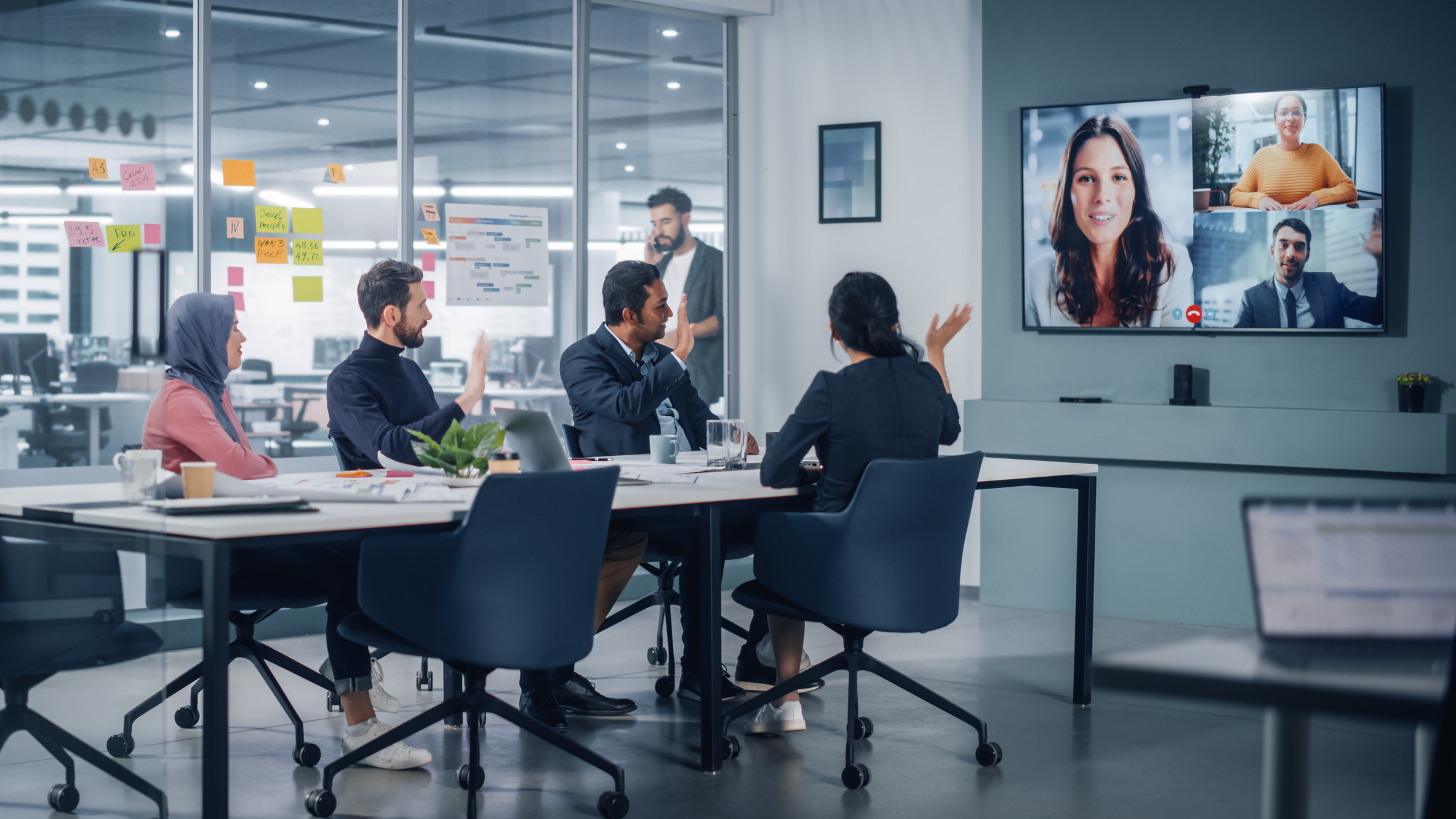 Four people in an office having a virtual meeting with three colleagues