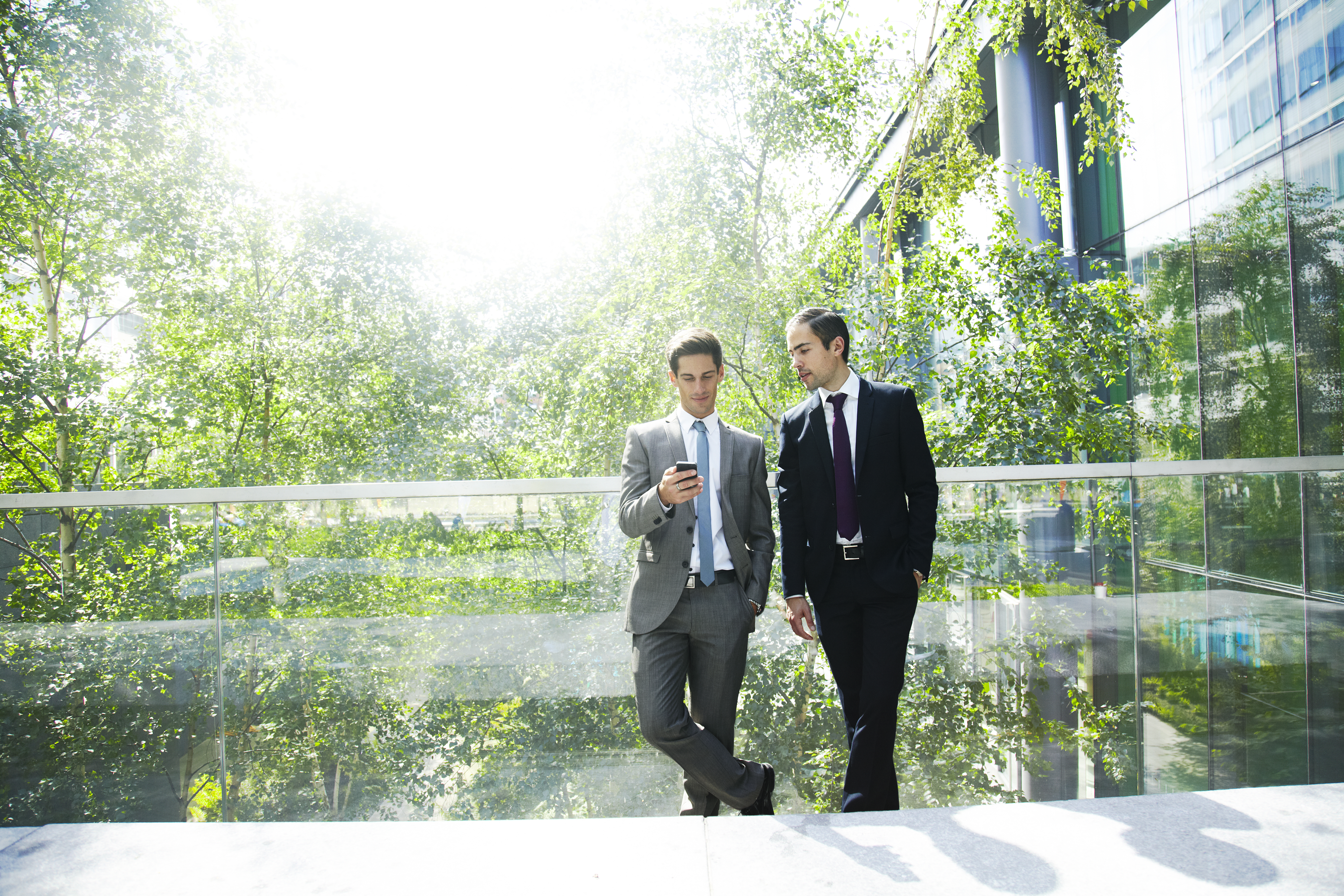 Two men looking at a phone while standing on a balcony in front of trees