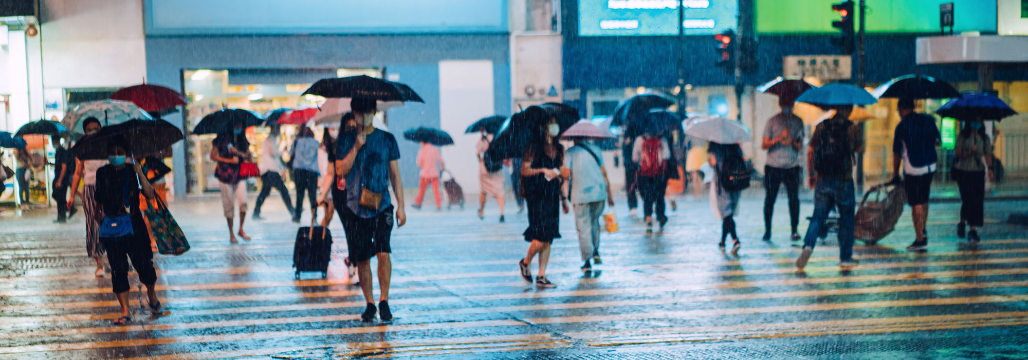Crowd of people carrying umbrellas crossing the street in heavy rain at night