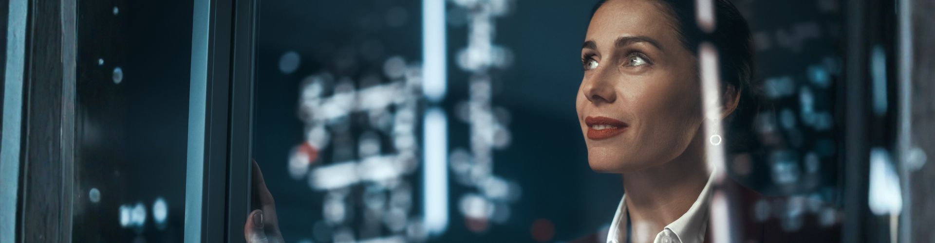 A woman in a blazer looking thoughtfully through a glass pane with digital bokeh in the background