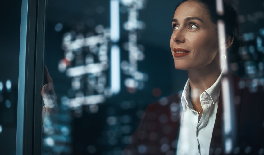 A woman in a blazer looking thoughtfully through a glass pane with digital bokeh in the background