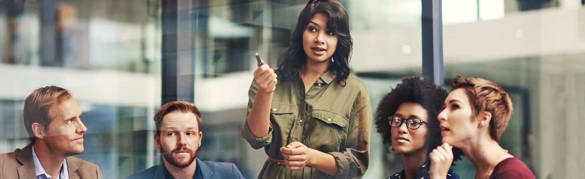 A woman standing up in a group of people pointing with her pen