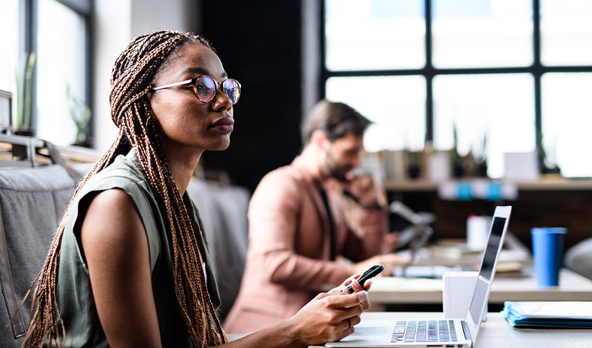 A black woman in glasses with braided hair sitting in front of a laptop