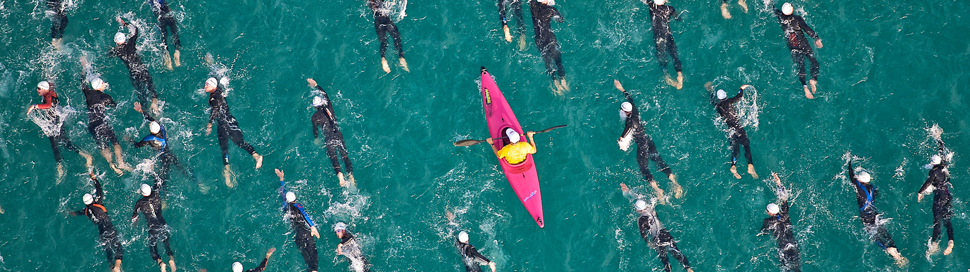 A pink kayak paddling among wet-suited sea swimmers