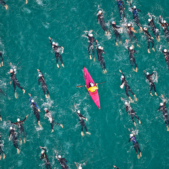 A pink kayak paddling among wet-suited sea swimmers