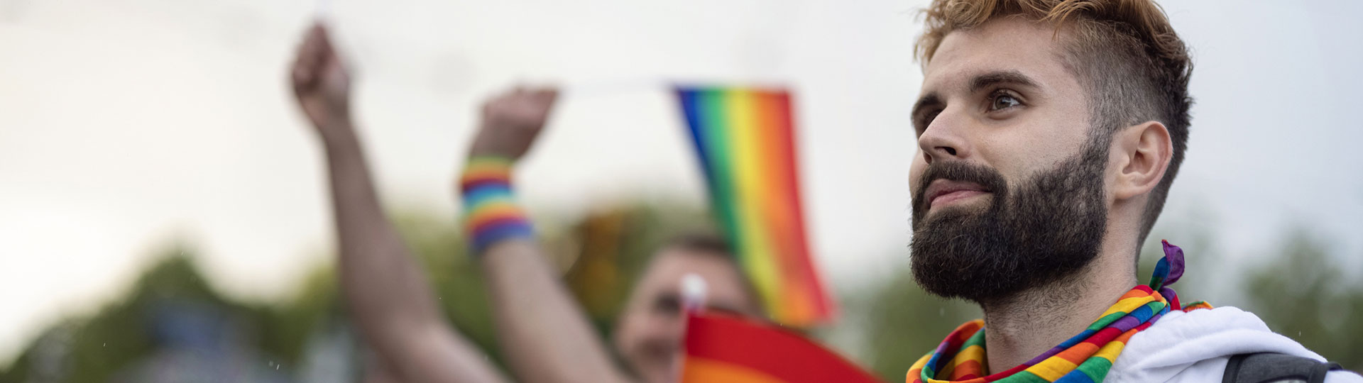A man in a crowd wearing a rainbow-coloured scarf