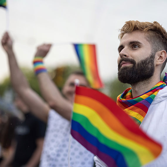 A man in a crowd wearing a rainbow-coloured scarf