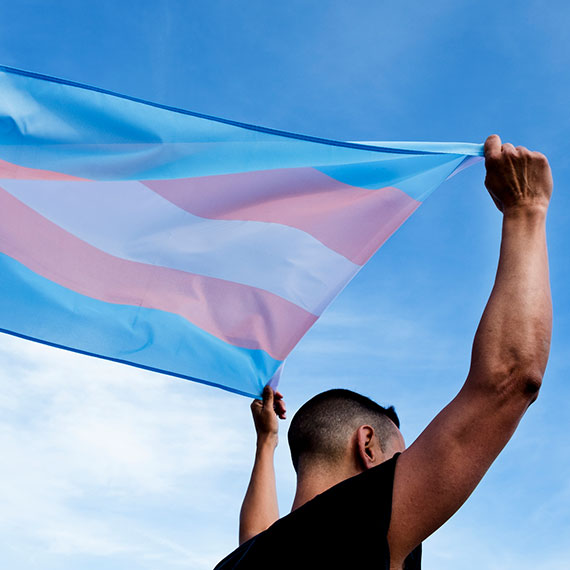 A person holding up the Transgender flag above their head
