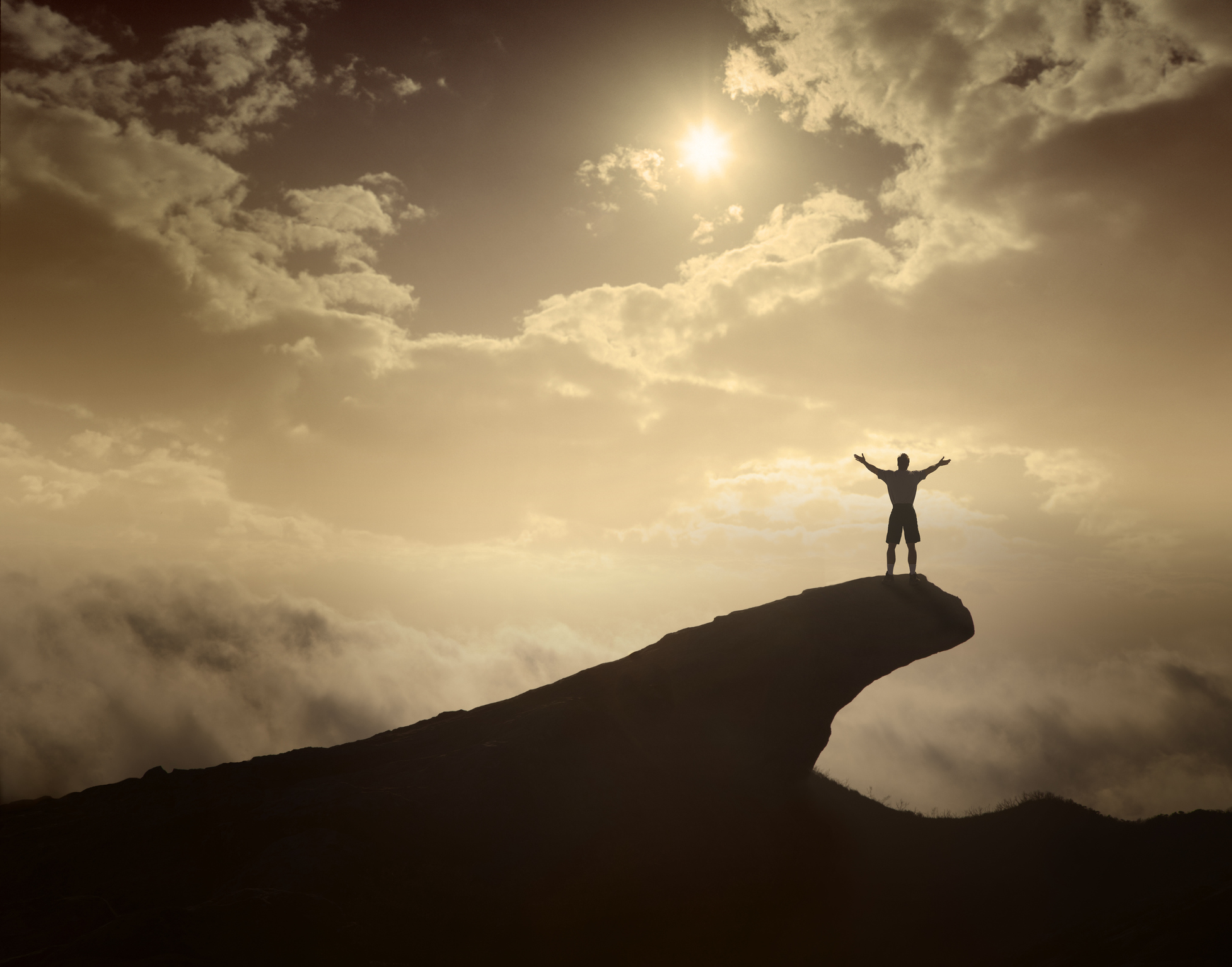 Man extending his arms on top of a cliff