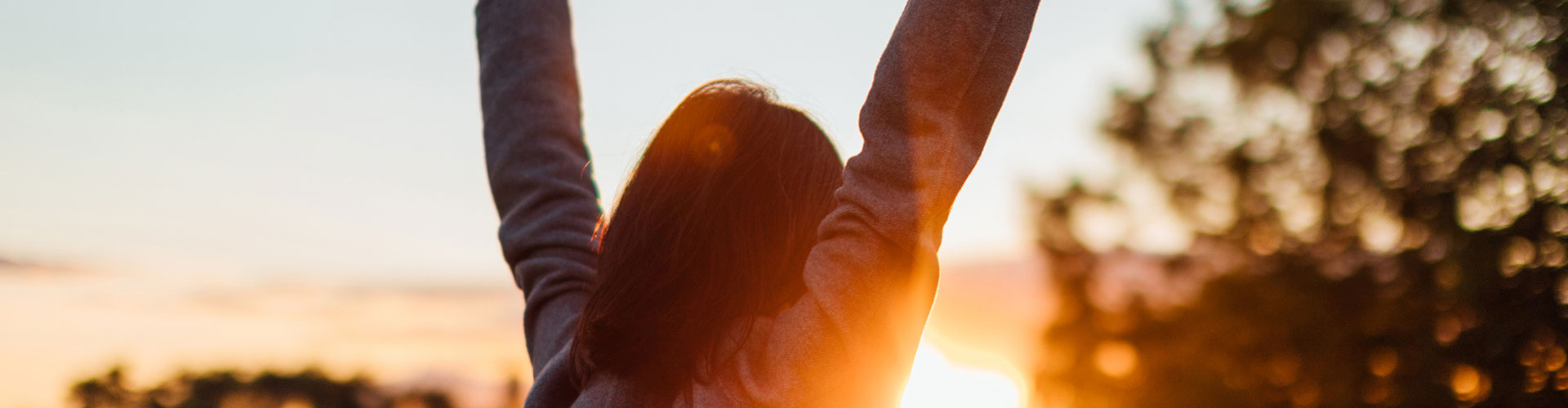 Rear view of young woman stretching arms against sunset in the sky