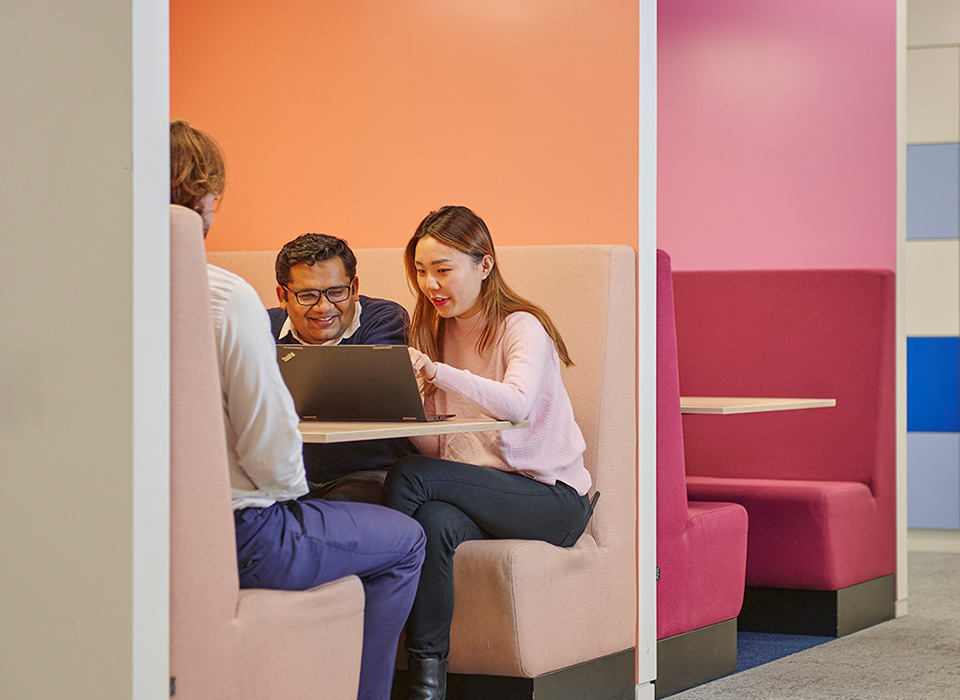 Colleagues sitting around a laptop in a booth
